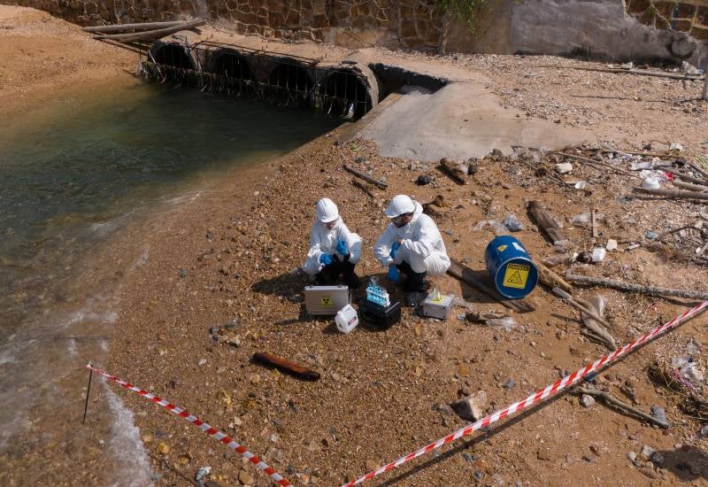 Environmental team in protective gear testing contaminated shoreline near a drain outlet in Houston